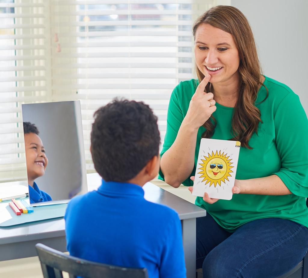 A child practicing speech sounds with a therapist using a mirror and picture cards